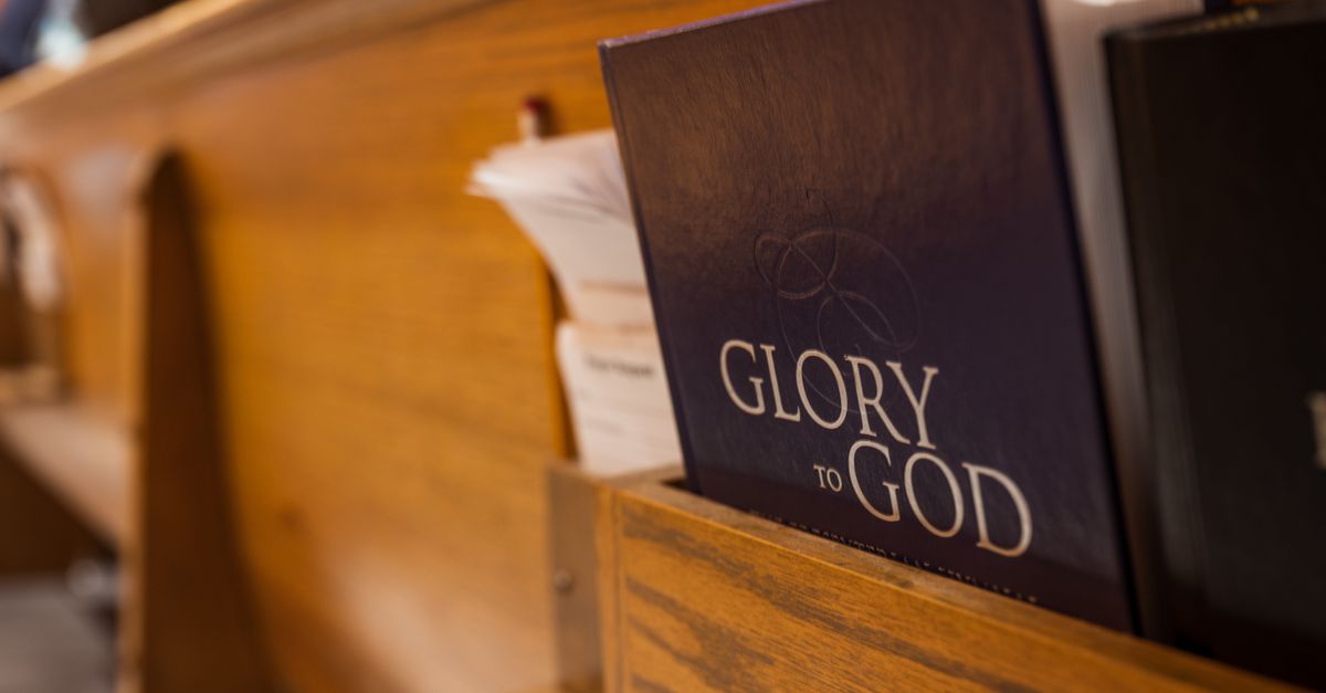 A hymnal titled 'Glory to God' placed in a church pew's book holder, capturing a religious atmosphere.